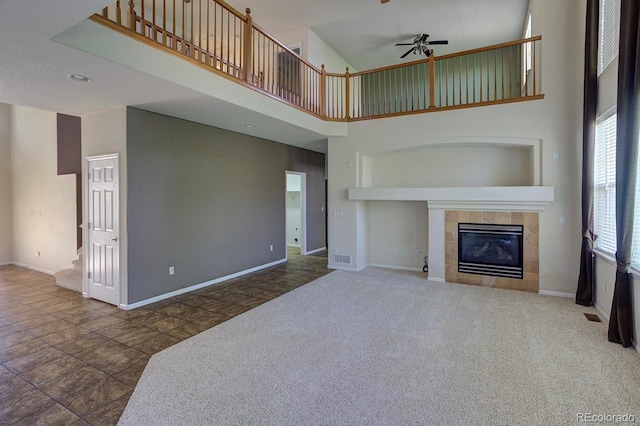 unfurnished living room with a towering ceiling, ceiling fan, a tiled fireplace, baseboards, and stairway