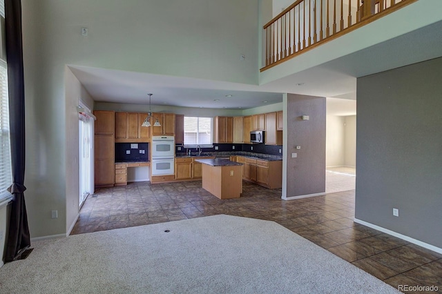 kitchen with stainless steel microwave, baseboards, a kitchen island, a high ceiling, and dark countertops