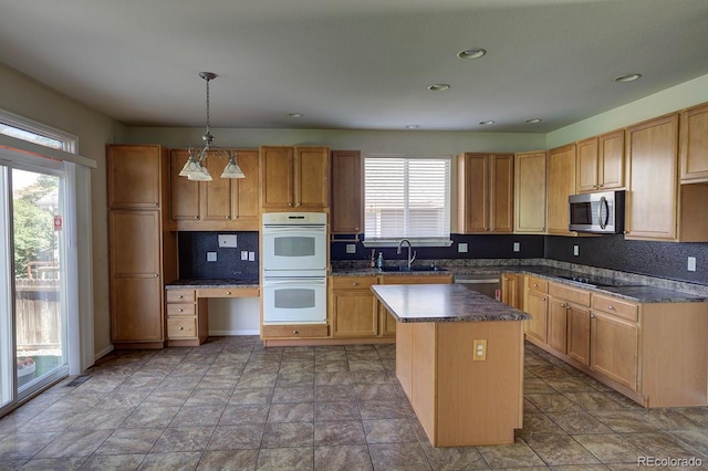 kitchen with appliances with stainless steel finishes, dark countertops, decorative backsplash, a sink, and a kitchen island