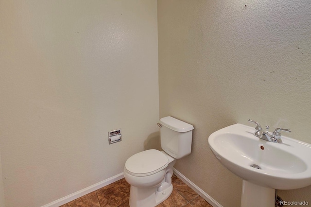 half bathroom with a sink, toilet, baseboards, and tile patterned flooring