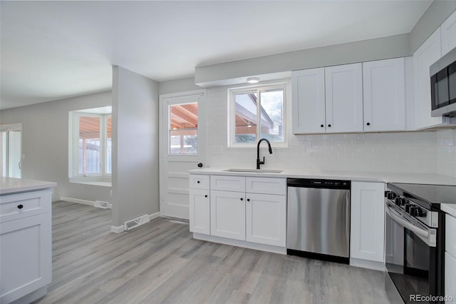 kitchen featuring sink, white cabinets, decorative backsplash, stainless steel appliances, and light hardwood / wood-style flooring