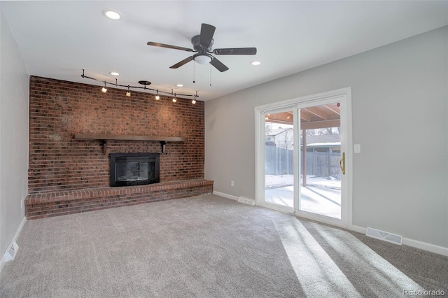 unfurnished living room featuring ceiling fan, rail lighting, carpet floors, and a brick fireplace