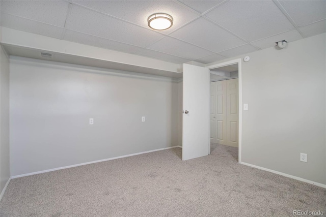 basement with a paneled ceiling and light carpet