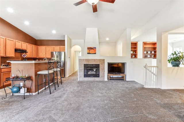 living room with lofted ceiling, ceiling fan, a tile fireplace, and light colored carpet