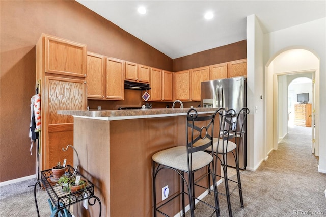 kitchen featuring light carpet, light brown cabinetry, vaulted ceiling, and a breakfast bar