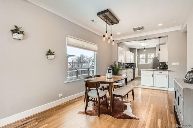 dining room with sink, crown molding, and light hardwood / wood-style flooring