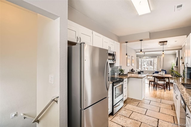 kitchen with appliances with stainless steel finishes, pendant lighting, white cabinetry, dark stone countertops, and kitchen peninsula