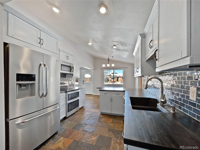 kitchen featuring vaulted ceiling, white cabinetry, sink, decorative backsplash, and stainless steel appliances