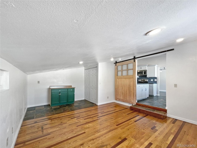 unfurnished living room with wood-type flooring, a barn door, and a textured ceiling