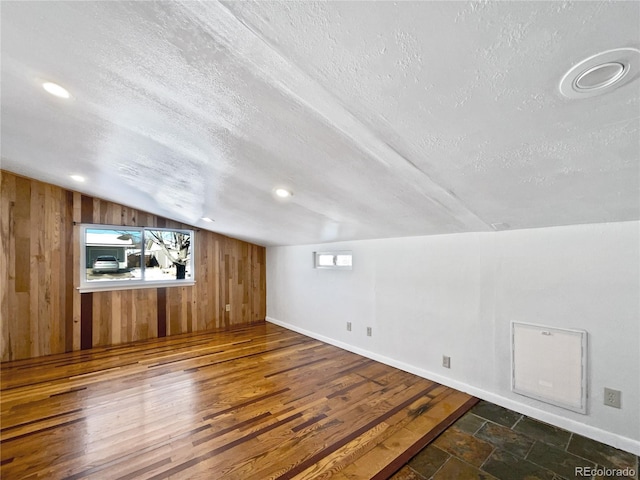 additional living space featuring wooden walls, vaulted ceiling, and a textured ceiling