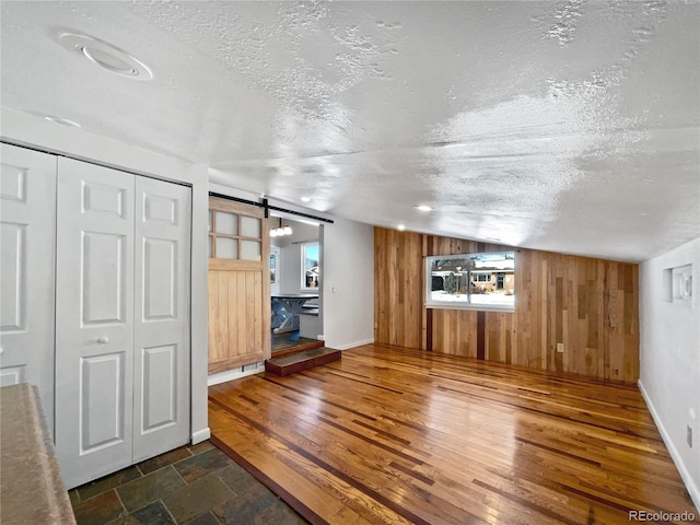 unfurnished living room featuring vaulted ceiling, a barn door, a textured ceiling, and wood walls