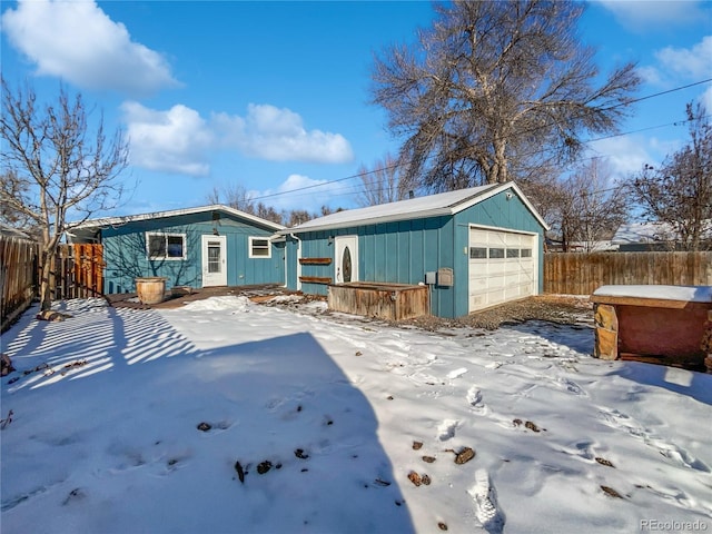 snow covered rear of property featuring a garage and an outbuilding