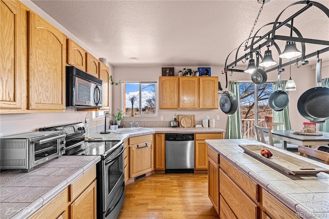 25 Tierra Casa Dr, Pueblo, CO 81005 - kitchen with sink, tile countertops, a textured ceiling, light wood-type flooring, and appliances with stainless steel finishes