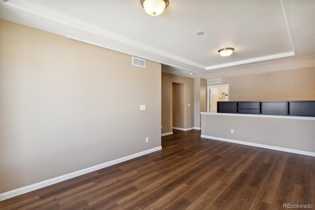 unfurnished room with baseboards, visible vents, a raised ceiling, and dark wood-style flooring