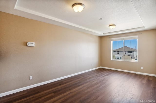 unfurnished room with a textured ceiling, a raised ceiling, baseboards, dark wood-style flooring, and visible vents