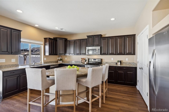 kitchen featuring a sink, a kitchen island, dark brown cabinetry, appliances with stainless steel finishes, and a breakfast bar area