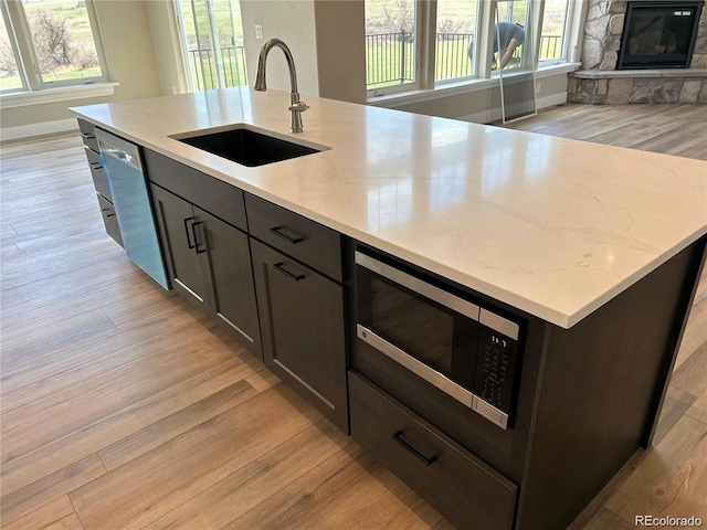 kitchen with light stone counters, sink, light hardwood / wood-style flooring, and appliances with stainless steel finishes