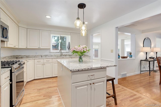 3090 S High St, Denver, CO 80210 - kitchen featuring stainless steel appliances, a kitchen island, light wood-type flooring, white cabinets, and hanging light fixtures