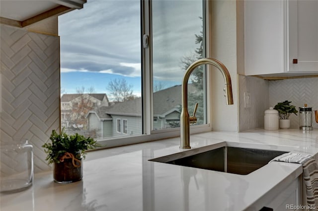 interior space with tasteful backsplash, white cabinetry, sink, and light stone countertops