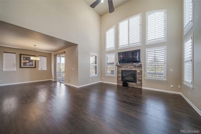 unfurnished living room with ceiling fan, dark wood-type flooring, a towering ceiling, and a stone fireplace