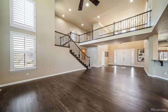 unfurnished living room featuring dark hardwood / wood-style flooring, ceiling fan, and a towering ceiling