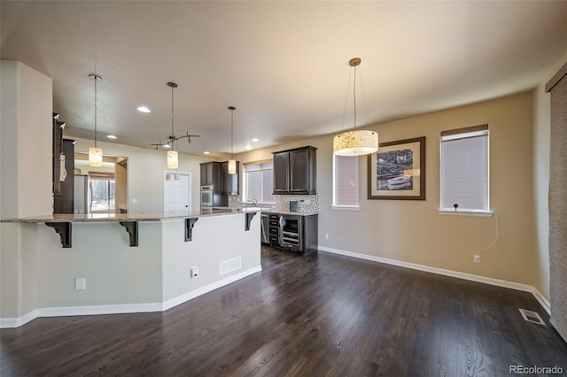 kitchen featuring pendant lighting, oven, dark hardwood / wood-style floors, light stone counters, and tasteful backsplash