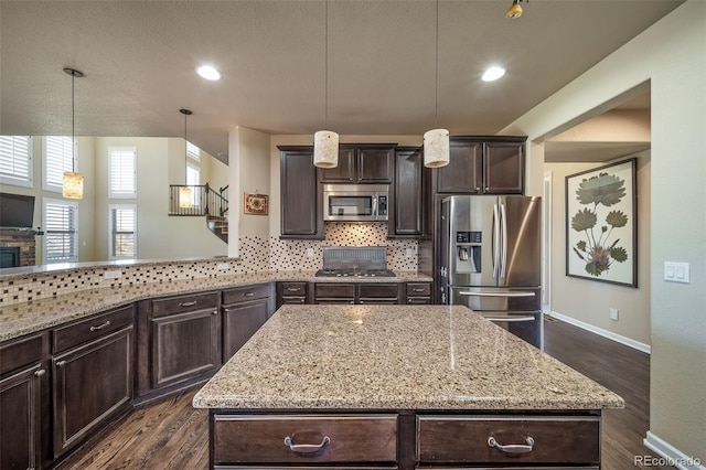 kitchen with dark hardwood / wood-style floors, backsplash, appliances with stainless steel finishes, light stone counters, and a kitchen island