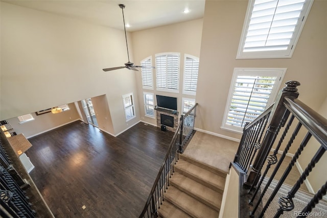 stairs with ceiling fan, a towering ceiling, and dark wood-type flooring