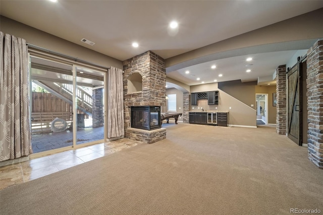 unfurnished living room featuring a fireplace, light carpet, and a barn door