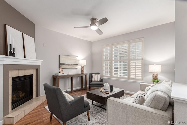 living area featuring a ceiling fan, wood finished floors, a fireplace, and baseboards