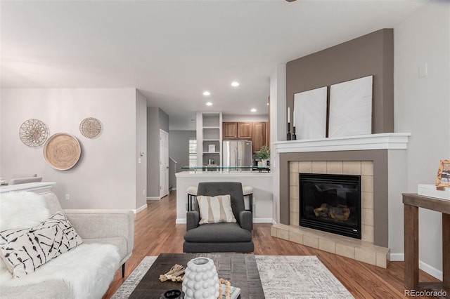 living area featuring recessed lighting, a tiled fireplace, light wood finished floors, and baseboards