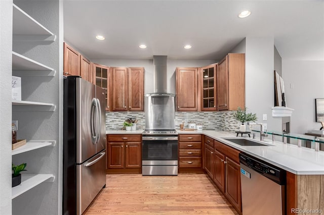 kitchen featuring open shelves, appliances with stainless steel finishes, a sink, wall chimney exhaust hood, and light wood-style flooring