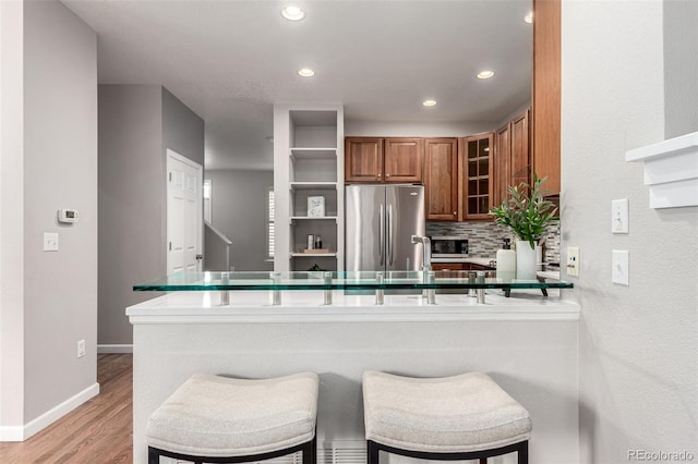 kitchen with appliances with stainless steel finishes, brown cabinets, glass insert cabinets, recessed lighting, and light wood-style flooring