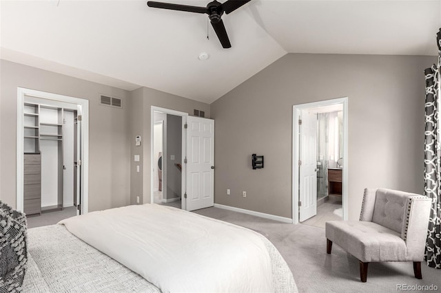 bedroom featuring lofted ceiling, light colored carpet, baseboards, a walk in closet, and ensuite bathroom