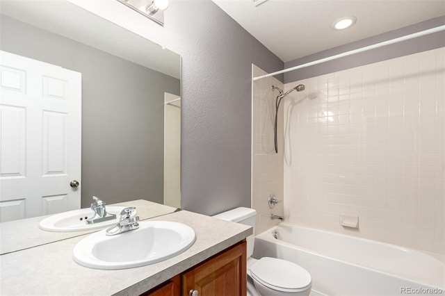 full bath with toilet, vanity, bathtub / shower combination, and a textured wall