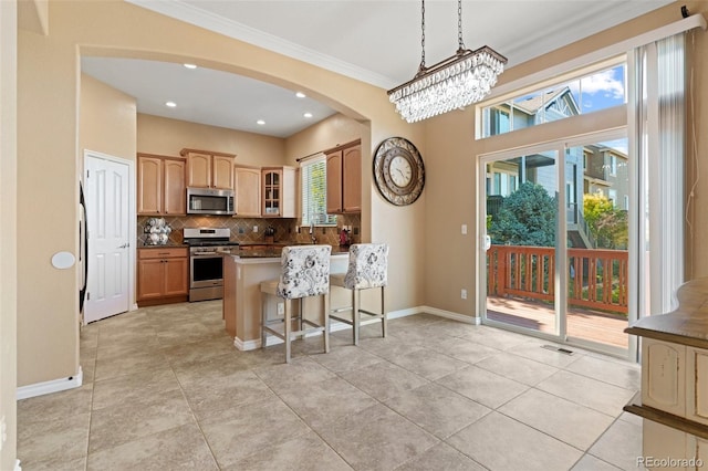 kitchen featuring a kitchen bar, appliances with stainless steel finishes, tasteful backsplash, crown molding, and a notable chandelier