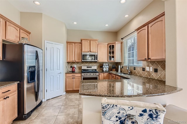 kitchen with sink, light brown cabinets, stainless steel appliances, kitchen peninsula, and dark stone counters