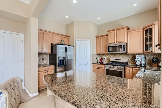 kitchen featuring tasteful backsplash, kitchen peninsula, stone counters, and appliances with stainless steel finishes