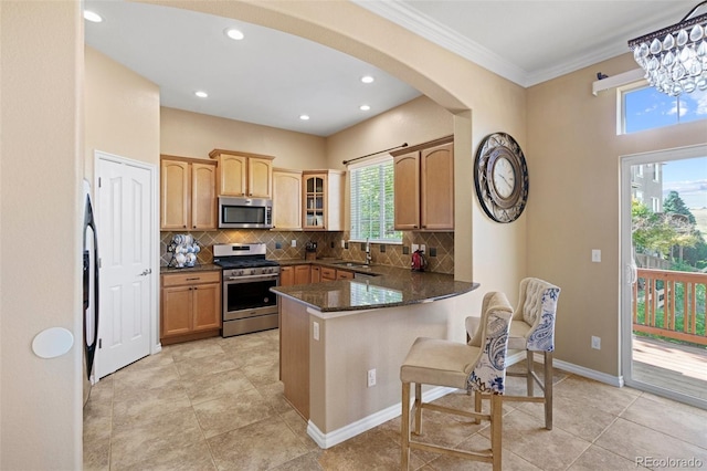 kitchen with sink, kitchen peninsula, dark stone countertops, appliances with stainless steel finishes, and ornamental molding