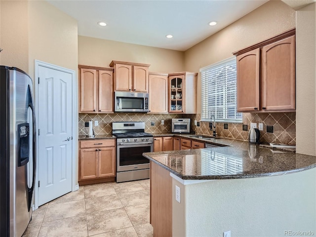 kitchen with dark stone counters, sink, light tile patterned floors, kitchen peninsula, and stainless steel appliances