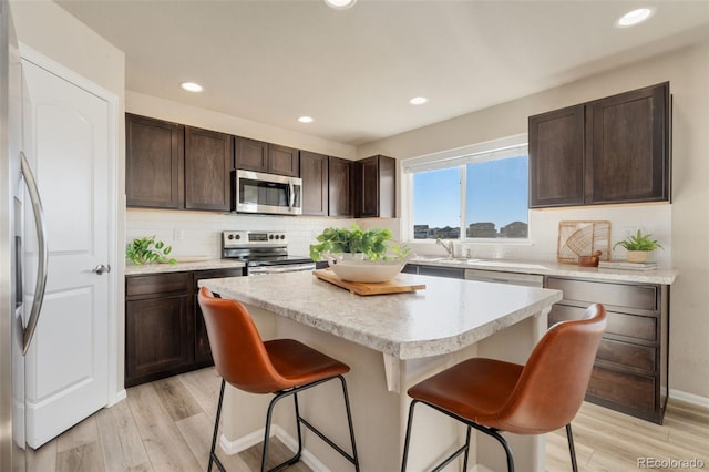 kitchen with stainless steel appliances, a kitchen bar, a center island, and light hardwood / wood-style flooring