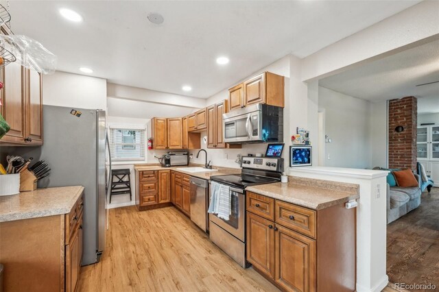 kitchen featuring appliances with stainless steel finishes, light wood-type flooring, a sink, light countertops, and brown cabinets