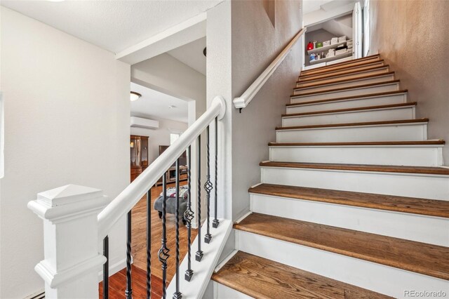 stairs featuring an AC wall unit and wood finished floors