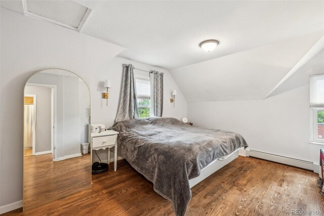 bedroom featuring a baseboard heating unit, wood finished floors, lofted ceiling, baseboards, and arched walkways