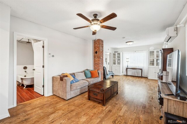 living area with a wall mounted air conditioner, light wood finished floors, and ceiling fan