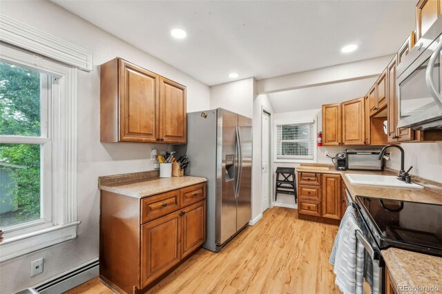 kitchen with stainless steel appliances, a sink, baseboard heating, light wood-type flooring, and brown cabinets