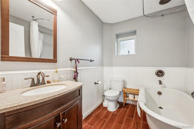full bathroom with a wainscoted wall, vanity, a freestanding bath, wood finished floors, and toilet