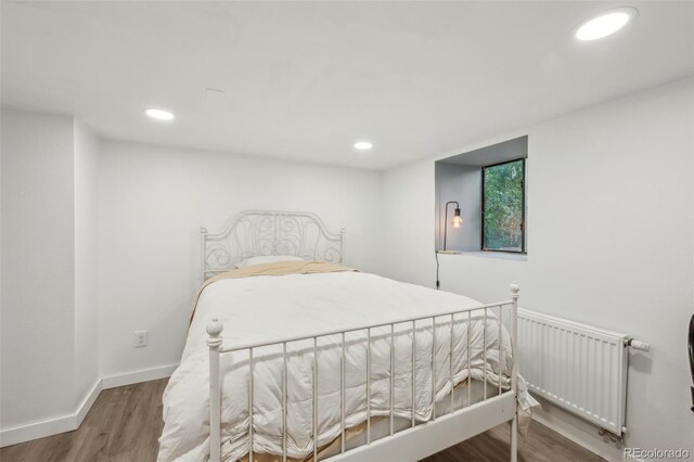 bedroom featuring radiator, wood finished floors, recessed lighting, and baseboards