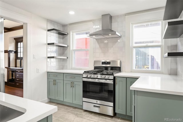 kitchen with gas range, wall chimney exhaust hood, green cabinets, light tile patterned floors, and tasteful backsplash