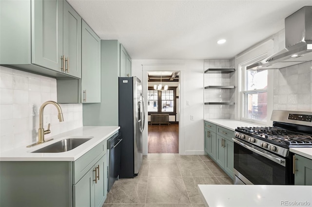 kitchen with stainless steel appliances, sink, green cabinetry, radiator, and wall chimney range hood